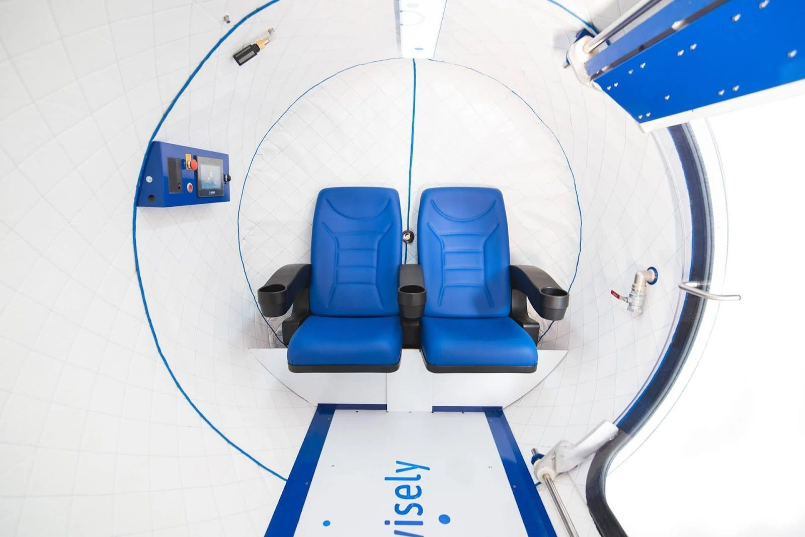 Interior of a futuristic space tourism capsule with two blue seats, a control panel, and windows for viewing, featuring a sleek and modern design with a focus on passenger experience and comfort.